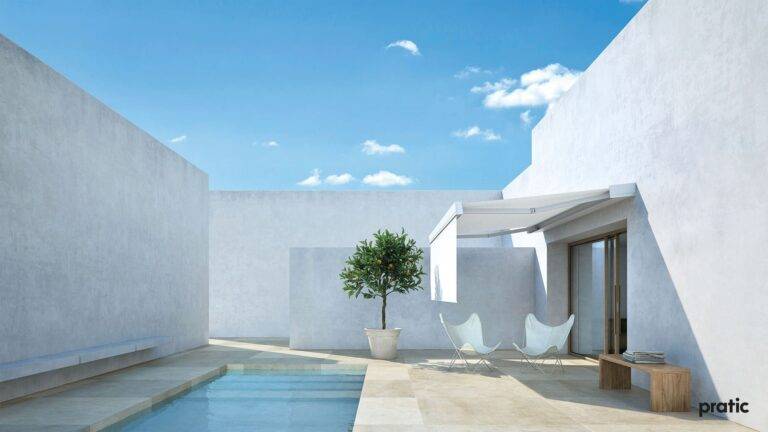 Helle, weiße Terrasse mit Pool und einem Bäumchen. Der Sitzbereich wird von einer weißen Markise beschattet.