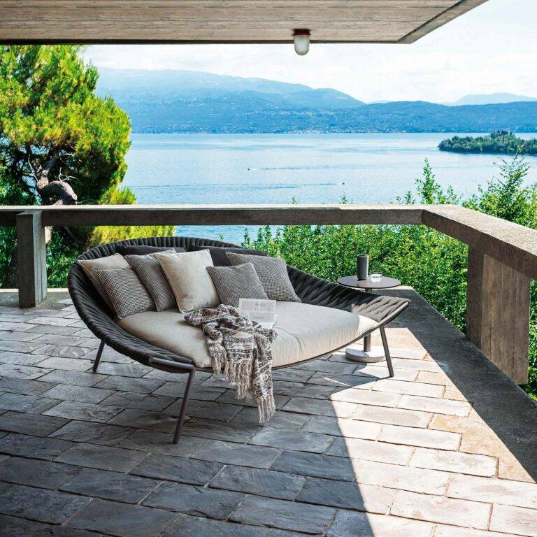 Outdoor-Sofa mit Kissen in der Farbe Grau und Beige auf der Terrasse. Strahlendes Wetter mit Blick auf das Meer.