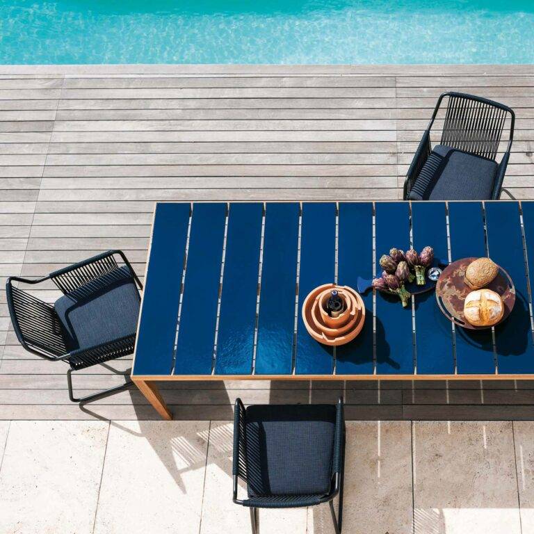 Blauer Gartentisch steht mit Stühlen am Rand des Pools.