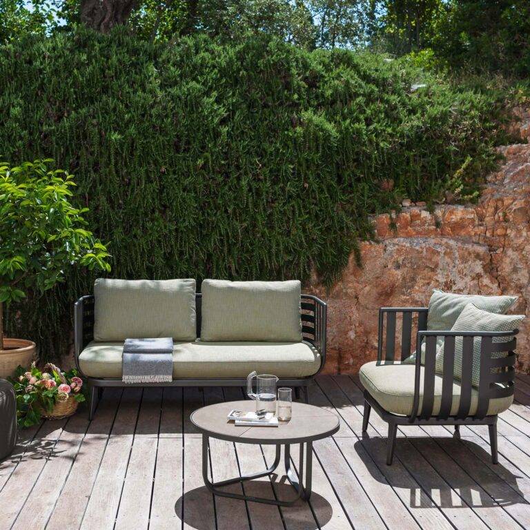 Couch, Sessel und Tisch auf einer Holzterrasse in der Sonne mit Bäumen im Hintergrund