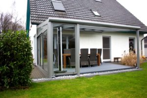 Moderne Terrassenüberdachung aus Glas mit seitlichen Glasschiebeelementen für optimalen Schutz und flexible Nutzung des Außenbereichs.